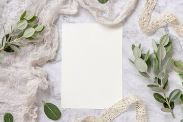 Blank paper card laying on a marble table decorated with eucalyptus branches
