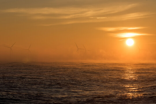 Misty sunrise over offshore windfarm. Beautiful tropical sky with wind turbines.