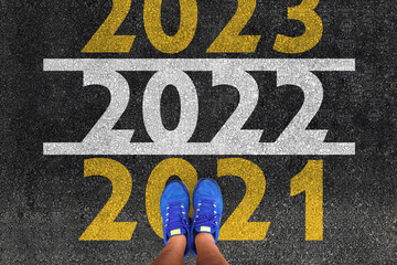 happy new year 2022. man legs in sneakers standing on asphalt road and number 2021 next to number...