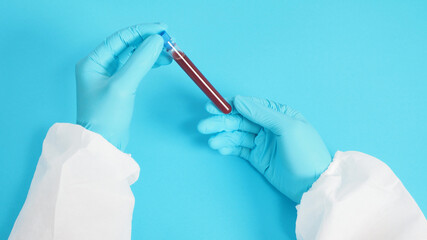 Hand with PPE suite and Hand is holding Blood test  tubes and wearing medical glove on blue...