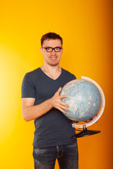 Puzzled young traveler tourist man in summer clothes holds the earth world globe put his hand on the holobus isolated on a yellow background. The passenger travels on weekends. Air travel concept 