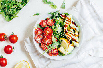 top view of tomato salad arugula avocado lemon in white plate on light background