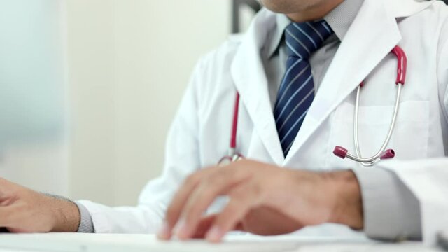 Young asian doctor working online texting on the keyboard video conference with team. Close Up Physician in white coat, stethoscope working with laptop