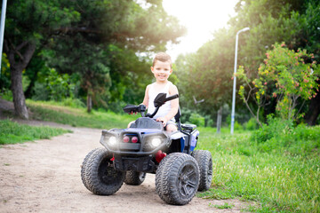 A cute five year old boy rides a black and purple ATV Quad bike in a summer park.	
