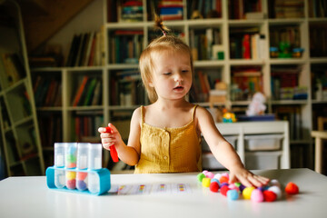Cute Caucasian child on the table plays with balls and test tubes, the child studies the color...