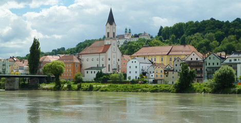 Fototapeta premium View over river Inn on hill with church (St. Gertraud) and monastery (Mariahilf) against cloudy sky - Passau, Germany (focus on center)