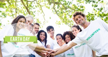 Composition of earth day text over diverse smiling volunteers making hand stack in countryside