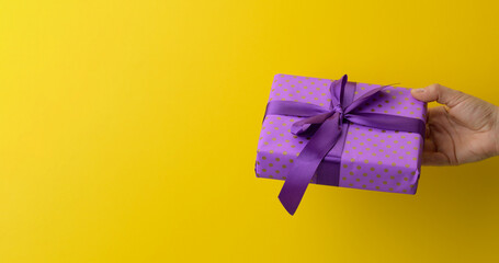 female hand are holding a purple gift box on a yellow background, happy birthday concept