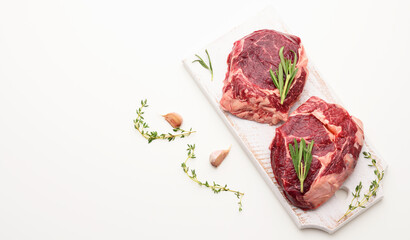 raw piece of beef ribeye with rosemary, thyme on a white table, top view