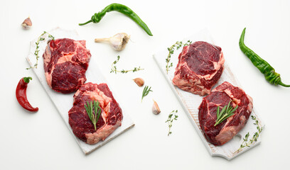 raw piece of beef ribeye with rosemary, thyme on a white table, top view