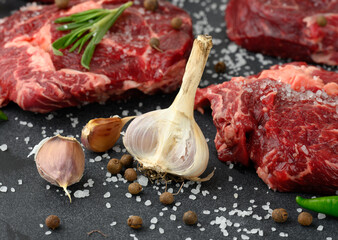 fresh garlic andraw piece of beef ribeye with rosemary, thyme on a black table
