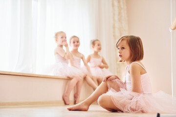 Obraz na płótnie Canvas Girls sits on windowsill and on the floor. Little ballerinas preparing for performance
