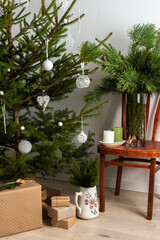 Christmas tree with white toys, old chair with a vase with pine branches, gift boxes under the tree, part of home interior