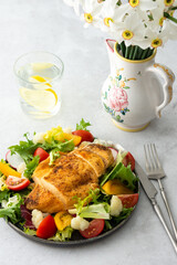 Delicious hearty lunch, chicken breast baked with spices and a mix of salad with tomatoes, radishes and cauliflower, a plate of salad and daffodils in a vase