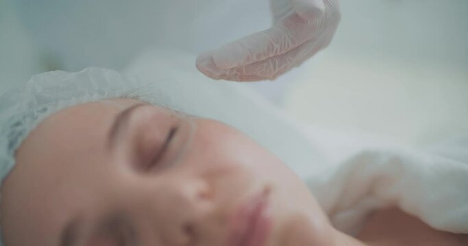 Close-up female face and cosmetologist is applying cream onto her face by using a cosmetic brush. Beauty procedure.