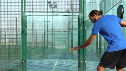 Slow motion of a professional paddle tennis player serving and running towards the net on an outdoor court.