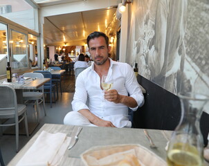 Przystojny, uśmiechnięty, dojrzały brunet z lampką wina podczas klimatycznej kolacji we włoskich klimatach.  - obrazy, fototapety, plakaty
