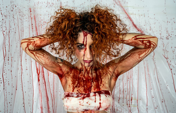 Bloodied skinny woman with her hands on her head surrounded by bloodstained plastic sheeting