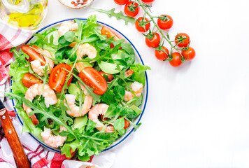 Shrimp salad with cherry tomatoes, arugula, avocado, and oil lemon dressing on white background. Top view