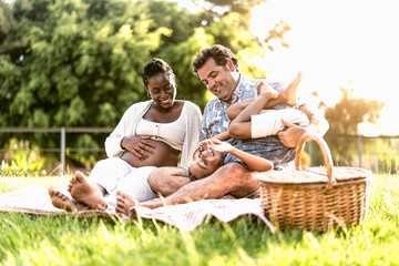 Playful multiracial family having fun in park doing a picnic together - Parents love concept