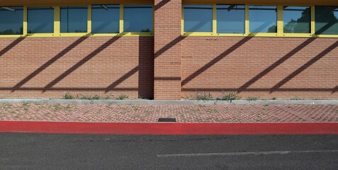 Brick wall with a row of windows. Tiled sidewalk and asphalt road in front. Background for copy space.