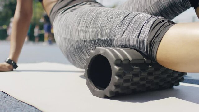 Young athletic female rolling her hamstring on a foam roller, in slow motion