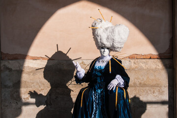 Female wearing a mask and blue carnival costume standing by the wall in Venice, Italy