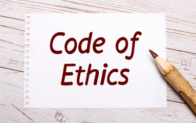 On a light wooden background, a colored pencil and a white sheet of paper with the text CODE OF...