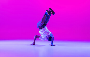 Fototapeta na wymiar One young stylish man, break dancing dancer training in modern clothes isolated over bright magenta background at dance hall in neon light.