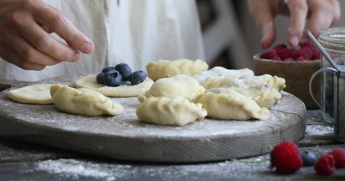 Woman made a homemade dumplings or Pierogi on wooden background with flour. Traditional Ukrainian or Polish food.