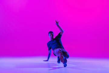 Young stylish man, hip-hop dancer dancing solo in modern clothes isolated over bright magenta background at dance hall in neon light.