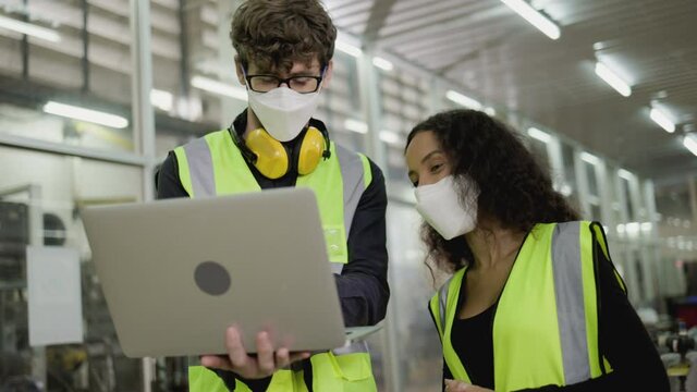 Technical team wears face mask to work laptop to checkup machinery in industrial factory. safety engineers working check on machines. Professional maintenance technology. health care of workers