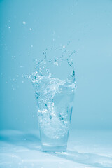 Naklejka na ściany i meble Ice cubes splashing into glass of water, isolated on white