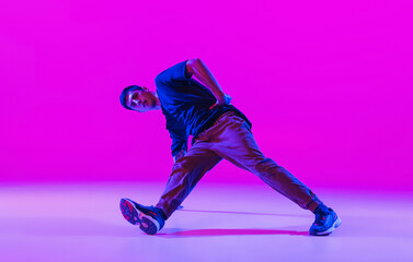One young stylish man, break dancing dancer training in modern clothes isolated over bright magenta background at dance hall in neon light.