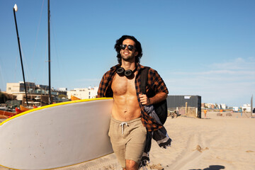 Portrait of handsome surfer with his surfboard. Young man with a surfboard on the beach.