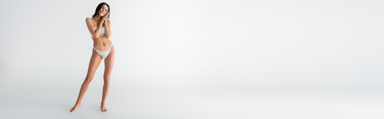 full length of young young joyful woman with closed eyes in lingerie posing on white, banner © LIGHTFIELD STUDIOS