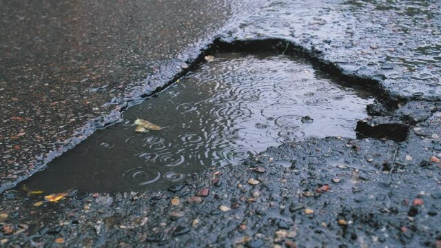 Hole in Damaged Asphalt Road Creating Water Puddle on Rainy Day