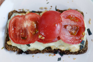 Rye bread sandwich with tomatoes, melted cheese, basil and chicken on a pink plate close-up