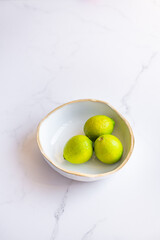 3 limes in a fruit bowl on marble surface