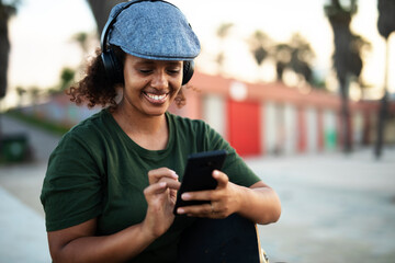 Portrait of happy african-american woman using the phone. Young stylish woman with skateboard outdoors.