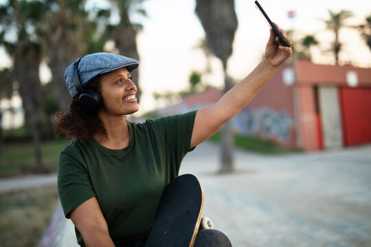 Portrait of happy african-american woman taking selfie photo outdoors. Happy woman sitting and listening the music.