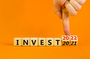 2022 invest and new year symbol. Businessman turns wooden cubes and changes words 'invest 2021' to 'invest 2022'. Beautiful orange background, copy space. Business, 2022 invest and new year concept.