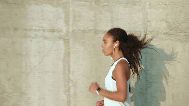 A concentrated african american athlete woman with earphones running outside in the morning