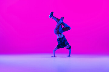 Fototapeta na wymiar Portrait of dancing man, break dancer in action, motion in modern clothes isolated over bright magenta background at dance hall in neon light.
