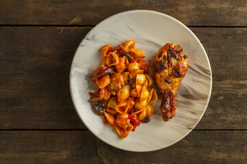 Seashell pasta in tomato with chicken leg baked on the grill on a wooden table.