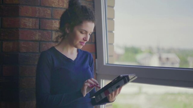 A young woman with a tablet is sitting by the window. View from the window.