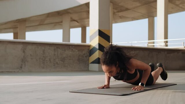 A muscular american woman doing push-ups on a yoga mat outside