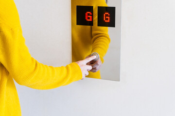 A woman in a yellow dress is pressing the G floor lift.