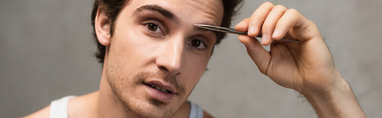 Obraz premium young man tweezing eyebrows in bathroom, banner