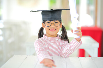 A little girl asia looks happy while celebrating his graduation and holding a diploma and graduation cap  which increases the development and enhances outside the classroom learning skills concept.